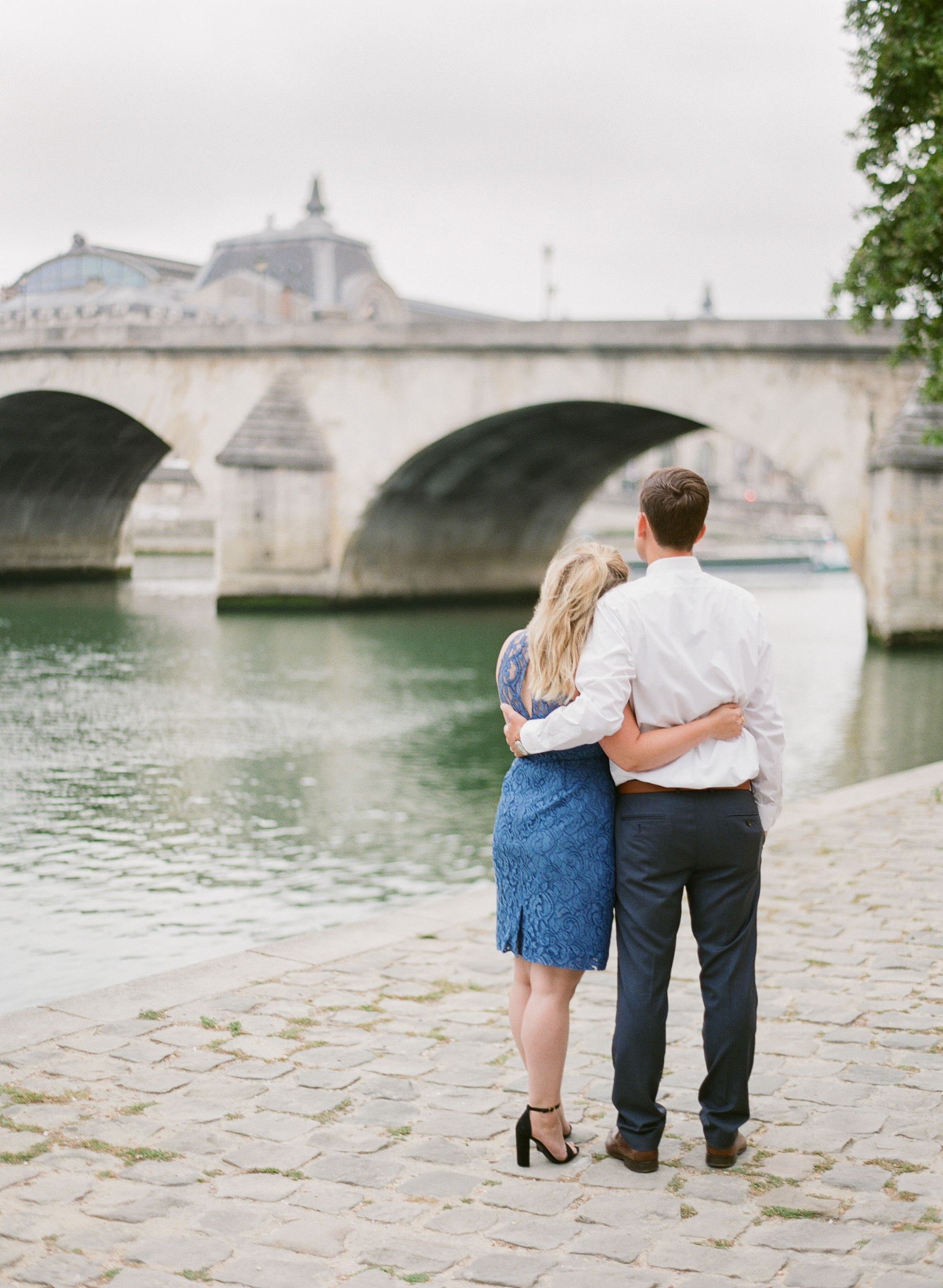 Paris Honeymoon Photographer | France Wedding Photographer | Paris Film Photography | Molly Carr Photography | Couple Standing By The Seine | Seine Engagement Photos | Girl In Blue Lace JCrew Dress